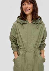 Helle olivgrüne Windjacke mit einer Kordelzugkapuze, elastischen Bündchen und verstellbarem Bund. Verfügt über große Seitentaschen und eine glatte Textur.