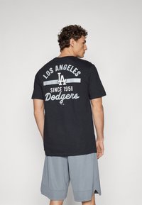 Black cotton t-shirt featuring "LOS ANGELES" and "Dodgers" in white and gray text on the back, with a relaxed fit and short sleeves.