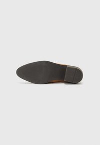 Chaussure en cuir suédé brun avec un bout lisse et effilé, semelle en caoutchouc noir plat et motif de traction subtil au bas.