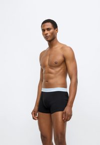 Μαύρα ανδρικά εσώρουχα boxer με ελαστική μέση σε ανοιχτό γαλάζιο και λογότυπο. Το ύφασμα φαίνεται λείο και εφαρμοστό.