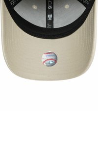 Gorra de béisbol beige con visera negra. Presenta un parche circular con un diseño de béisbol en la parte frontal. Tela texturizada y detalles en el forro interior.