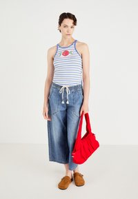 Pasi z rešenim naramnicami v modro-beli črti z grafiko jabolka, široke modre denim culotte hlače in rdeča torba za ramo. Rjavi natikači.