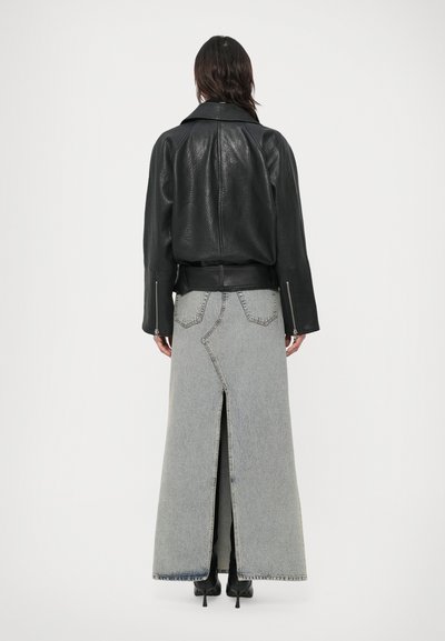 Casaco de couro preto com ombros estruturados e mangas compridas, combinado com uma saia de ganga cinza de cintura alta com uma abertura central.