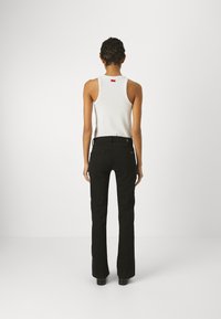 Pantalones de campana negros con una textura suave, con cierre de botón metálico, dos bolsillos traseros y una sutil etiqueta de logo cerca de la cintura.
