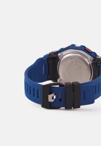 Blå silikonarmband till klocka med ribbad textur, försett med en svart spänne och en baksida av rostfritt stål med ingraverade detaljer.