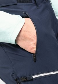 Marineblaue Hosen aus glattem Stoff verfügen über eine seitliche Reißverschlusstasche mit kontrastierendem weißen Reißverschluss. 