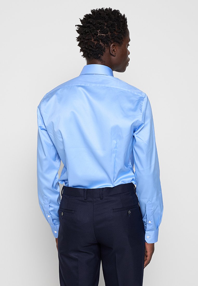 Helles blaues, langärmliges Hemd mit strukturiertem Kragen, glatter Textur und geknöpften Manschetten, kombiniert mit dunkel gemusterten Hosen.