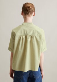 Camicetta a maniche corte in cotone verde chiaro, con un dettaglio a pieghe sul retro, colletto classico e vestibilità rilassata.