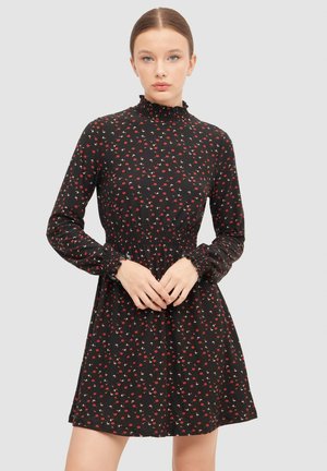 Vestido negro con flores rojas y acentos blancos, mangas largas con puños fruncidos, alto cuello ajustado, cintura ceñida y falda acampanada.