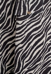 Čierno-biely textil s vzorom zebrových pruhov v tvare cik-cak. Na ľavej strane je vidieť zlatý gombík, ktorý pridáva kovový akcent.