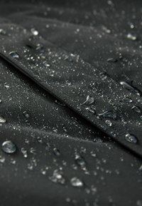 Tela negra impermeable con gotas de agua visibles en la superficie, mostrando una textura suave y un diseño en capas.