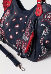 Granatowa skórzana torebka z czerwonymi akcentami i wyszukanym haftem w wzór paisley. Posiada odpinany pasek i błyszczące metalowe detale.