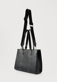 Fekete bőrből készült táska kontrasztos fehér varrással, két fogóval és levehető vállpánttal, amely logós díszítéssel rendelkezik.