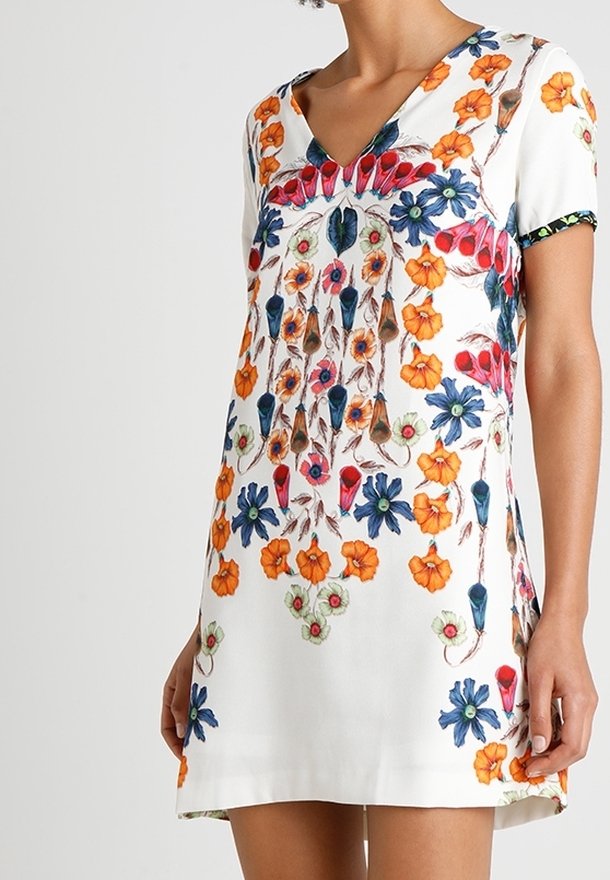 Robe courte blanche à manches courtes avec un imprimé floral vibrant en orange, bleu et rouge. Col en V avec des détails de motif le long des manches.