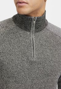 Grå halv-zip genser med et teksturert strikkemønster, stående krage og en glidelås ved halsen for justerbar komfort.