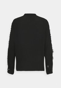 Chemise noire à manches longues avec bords effilochés aux manches et au col. Tissu doux, coupe décontractée, et fentes sur les côtés à l'ourlet.