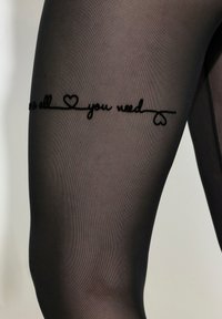 Černé průhledné punčochy s designem textu ve stylu ručního psaní na stehně, který říká "Vše, co potřebuješ," doplněný malým srdíčkem.