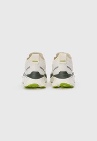 Pair of white athletic shoes with black and green soles, viewed from the back on a plain white background.