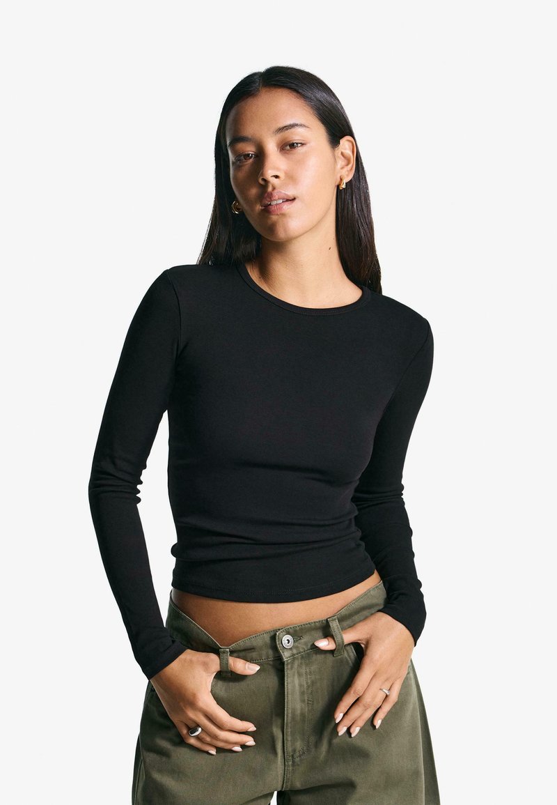 Black long-sleeve top made from soft fabric with a fitted design and round neckline. Paired with olive green trousers, showcasing a casual style.