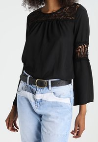 Czarna bluzka z koronkowymi detalami przy dekolcie i rękawach, zestawiona z jasnoniebieskimi dżinsami i czarnym paskiem ze złotą klamrą.