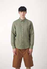 Camicia verde oliva a maniche lunghe con colletto, bottoni frontali e ricamo discreto del marchio, abbinata a pantaloni cargo marroni.