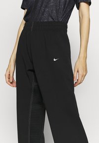 Czarne spodnie sportowe z elastycznym pasem, białym logo Nike oraz teksturowanym bocznym panelem z pionowymi pasami dla dodatkowego detalu.
