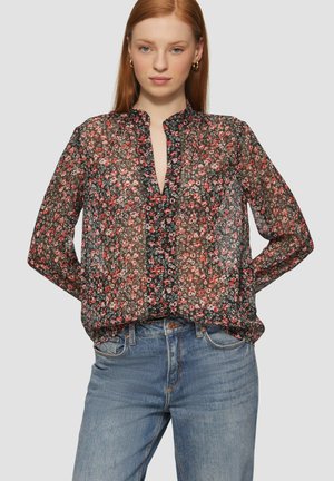 Schwarze transparente Bluse mit rot-weißer Blumenmuster, langen Ärmeln, lockerer Passform und einem Schlüsselloch-Ausschnitt. Kombiniert mit hellblauen Jeans.