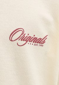Ύφασμα σε κρεμ χρώμα με τη λέξη "Originals" σε κόκκινη γραφική γραμματοσειρά και το "EST. 1990" τυπωμένο κάτω δεξιά.