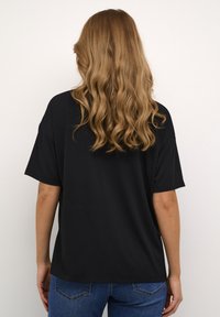Čierne oversized tričko z bavlny s voľným strihom, krátkymi rukávmi a rovnými lemami. Skombinované s modrými džínami viditeľnými v páse.