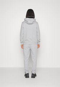 Grijze hooded sweatshirt en bijpassende joggers van zacht materiaal, met ribgebreide boorden en een relaxte pasvorm, gedragen met zwarte sneakers.