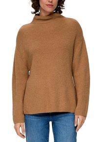 Brauner, grob gestrickter Pullover mit hohem Kragen, lockerer Passform und gerippter Textur, kombiniert mit blauen Jeans. Die Ärmel sind lang und leicht oversized.