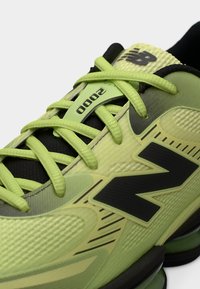 Πράσινο και μαύρο παπούτσι τρεξίματος New Balance 2000 με ορατά κορδόνια και λογότυπο της μάρκας στο πλάι και στη γλώσσα.