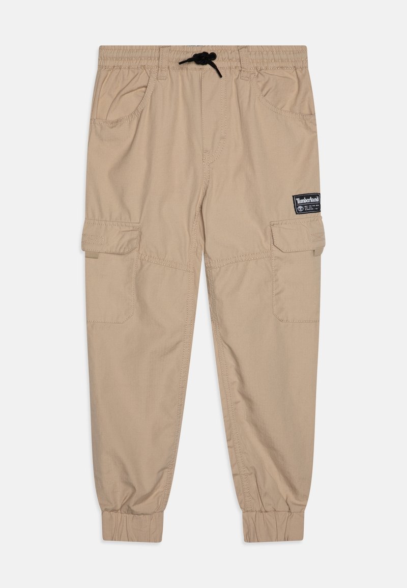 Beige cargobroek met een elastische tailleband en verstelbare trekkoord. Heeft meerdere zijzakken en geribbelde boorden bij de enkels.