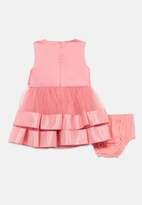 Ροζ φόρεμα με σατέν κορσέ και πολλαπλά επίπεδα τούλινης φούστας, με πτυχές. Περιλαμβάνει ταιριαστά ροζ κοντό παντελόνι. Κλείσιμο με φερμουάρ στο πίσω μέρος.