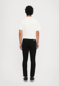 Melna džinsu bikses ar šauru piegriezumu, apvienojot ar vienkāršu baltu T-kreklu. Iespējas ietver uzlīmi uz aizmugurējā jostasvietas un baltas sporta apavus.