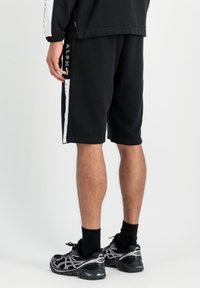 Shorts de sport noirs avec une texture lisse, ornés de rayures blanches sur les côtés et de marques. Associés à des baskets et des chaussettes noires.