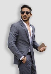 Gray tailored suit with a white shirt and dark sunglasses. Holding a brown wallet, featuring a textured finish. Simple black belt.