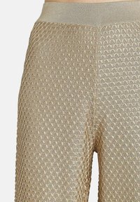 Gros plan sur un pantalon en tricot beige texturé avec un motif en losanges et une ceinture élastique lisse.