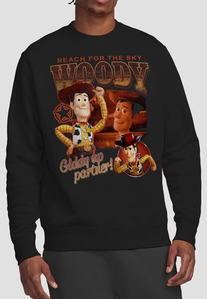 Man wearing black sweatshirt with three Woody cowboy character images, text "Reach for the sky" and "Giddy up partner!" in western style.
