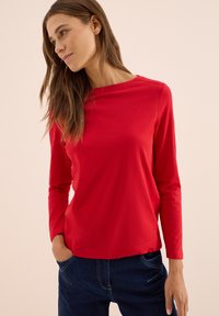 Röd långärmad t-shirt i mjuk bomull, med rund halsringning och en avslappnad passform, tillsammans med mörka denimjeans.