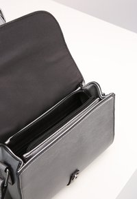 Borsa a tracolla in pelle grigia con chiusura a scatto magnetico, dotata di un compartimento con zip e una fodera interna liscia.