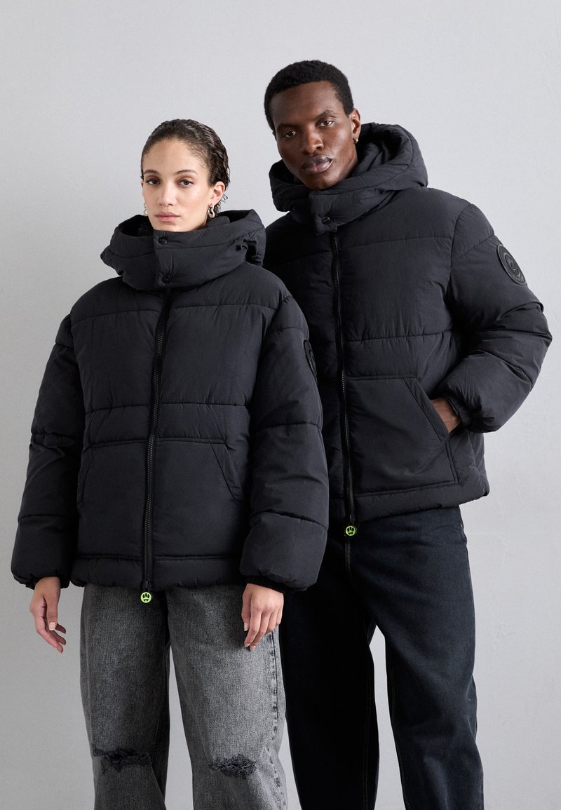 Black puffer jackets with high collars and zip closures, featuring quilted patterns and side pockets. Both have drawstring accents at the hem.