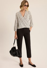 Bluzka z wzorem w czerni i bieli z rękawami 3/4, w połączeniu z czarnymi spodniami do kostek i dużą czarną skórzaną torbą.