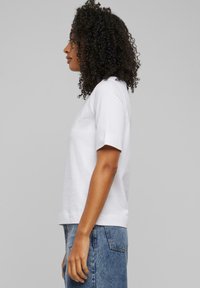 Weißes Baumwoll-T-Shirt mit kurzen Ärmeln, lockerer Passform und Rundhalsausschnitt. Kombination mit blauen Jeans, zeigt einen einfachen, lässigen Look.