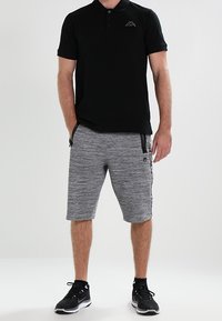 Svart pikétröja med krage och liten logotyp, i kombination med grå texturerade shorts med sidfickor och en kontrasterande sidremsa.