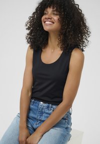 Schwarzes ärmelloses Oberteil mit Rundhalsausschnitt, kombiniert mit hoch taillierten hellblauen Jeans. Das glatte Material und das figurbetonte Design betonen die Silhouette.