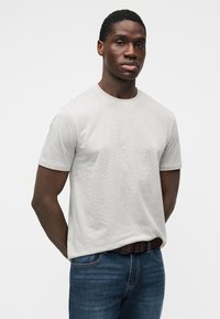 Camiseta de manga corta de color gris claro con un patrón texturizado. Modelo vistiendo jeans azul oscuro, mostrando el estilo casual de la camiseta.