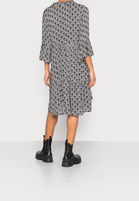 Robe à motifs noir et blanc avec des manches évasées, à hauteur du genou, fabriquée en tissu léger. Saison avec des bottines noires à semelle épaisse.