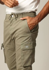 Khaki cargobroek gemaakt van lichtgewicht stof, met een elastische tailleband, trekkoord en zijzakken met een label op de dij.