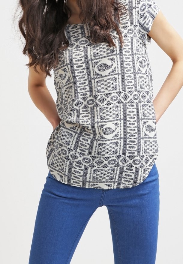 Kurzärmliges, gemustertes Oberteil in Creme und Marineblau mit geometrischen Designs. Kombiniert mit engen blauen Jeans. Sanfter Stoff und abgerundeter Saum.